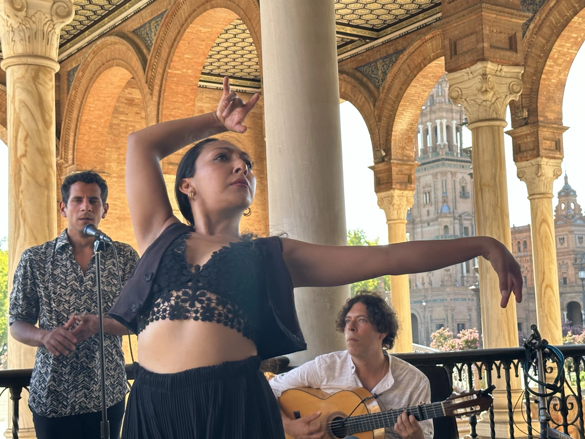 A flamenco dancer with two musicians beneath the brick arches of Plaza de España