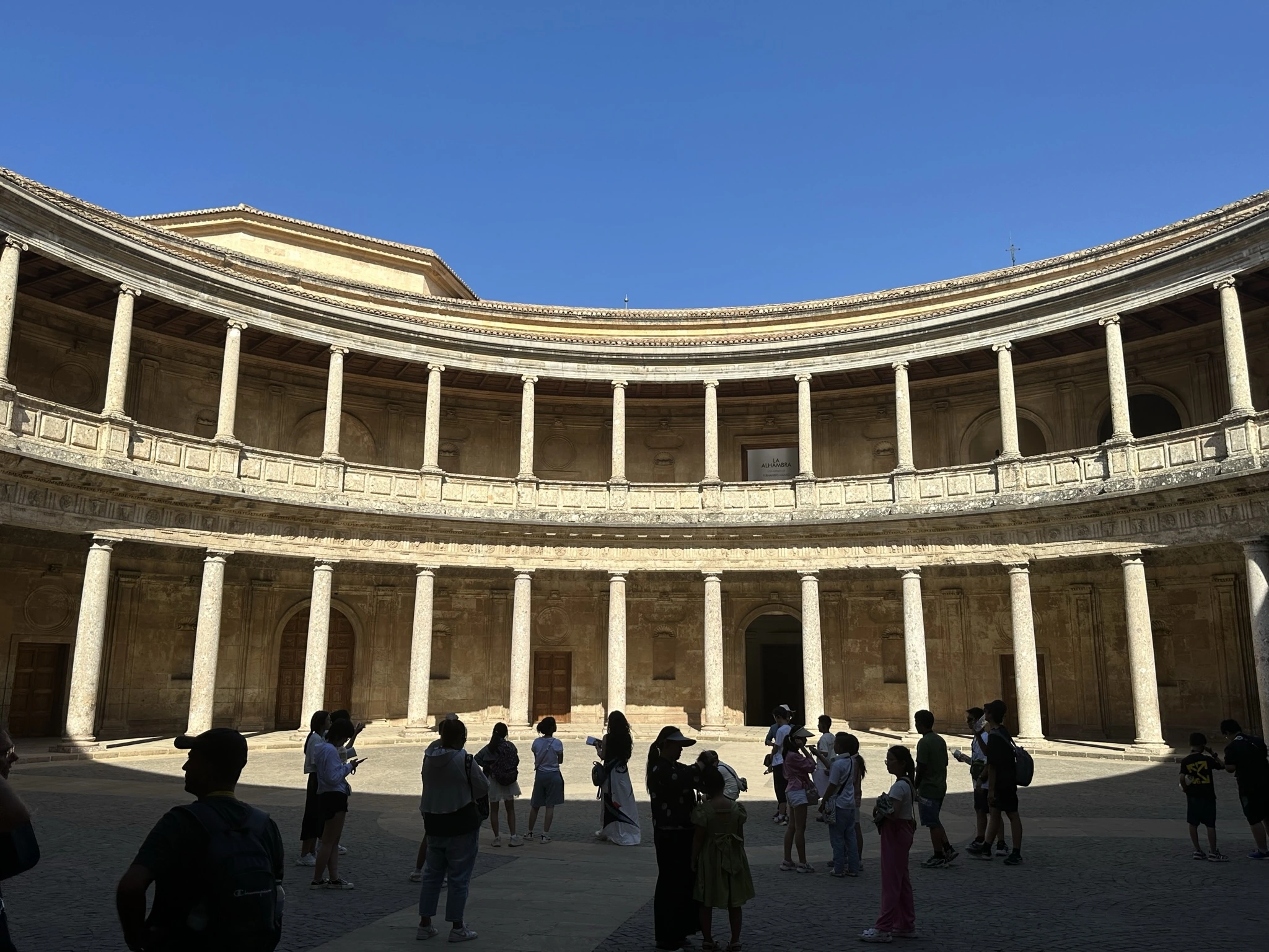Visitors in shadow beneath the curved colonnade of the Palace of Charles V