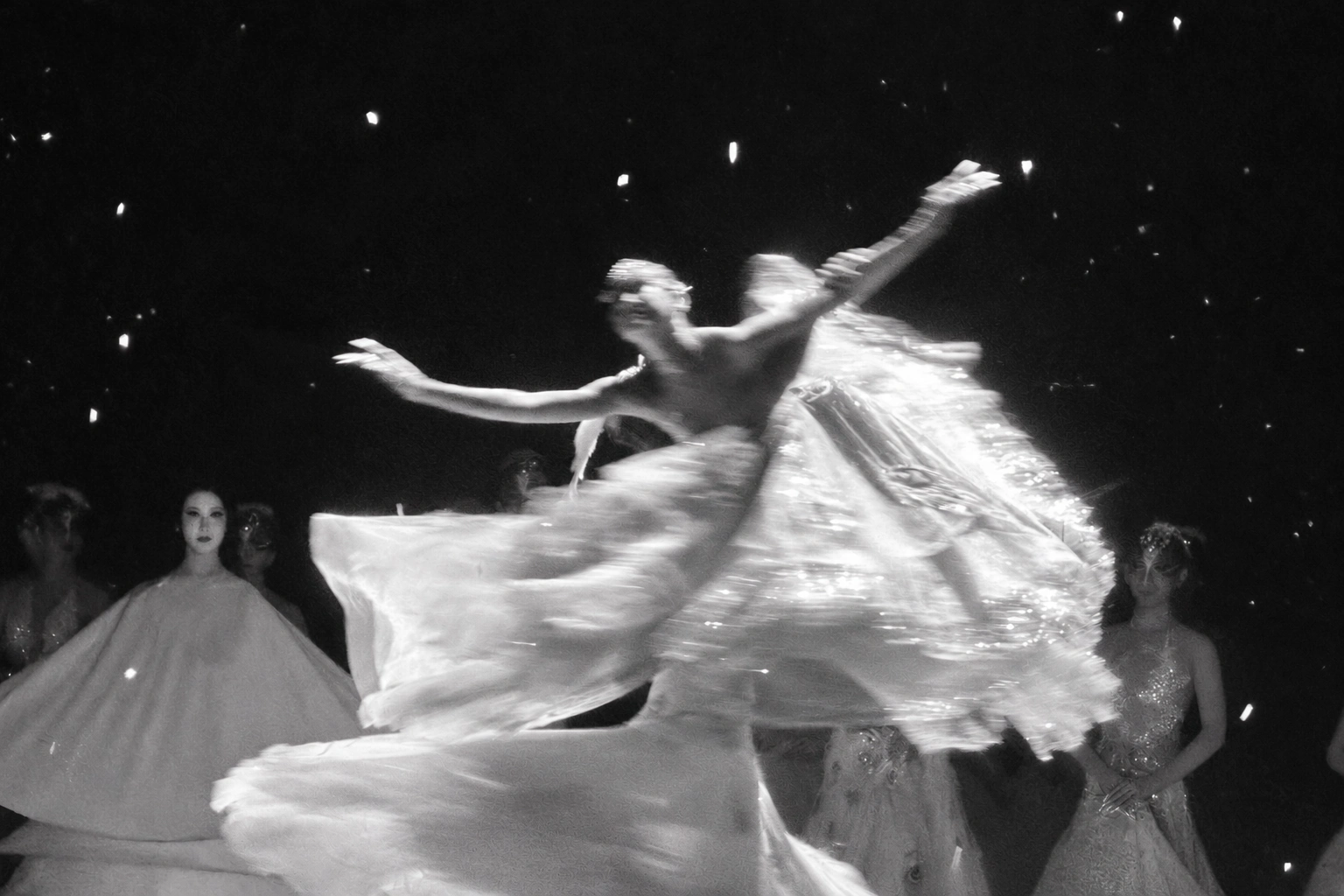 A dancer turns, with slow-shutter movement tracing the flowing fabric against a dark stage.